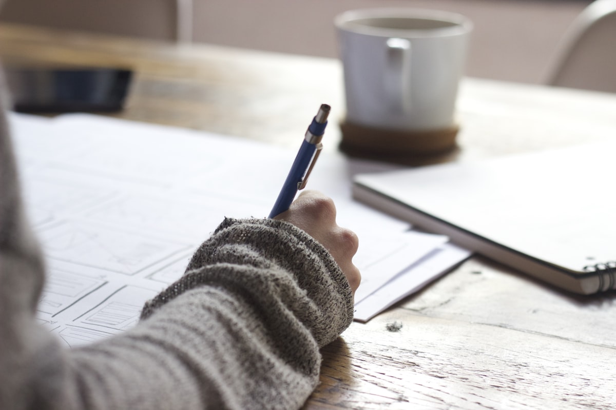 Researcher drafting notes beside books while writing a computing thesis